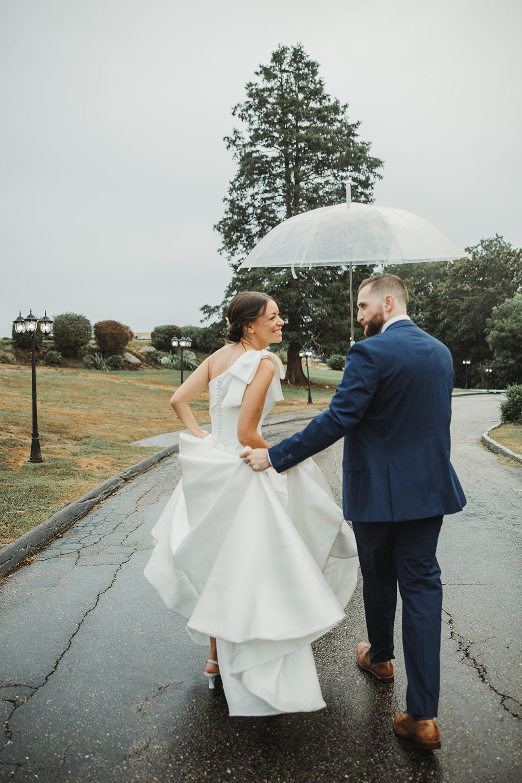 Bride and Groom Walk Under Clear Umbrella During Rainy CT Wedding