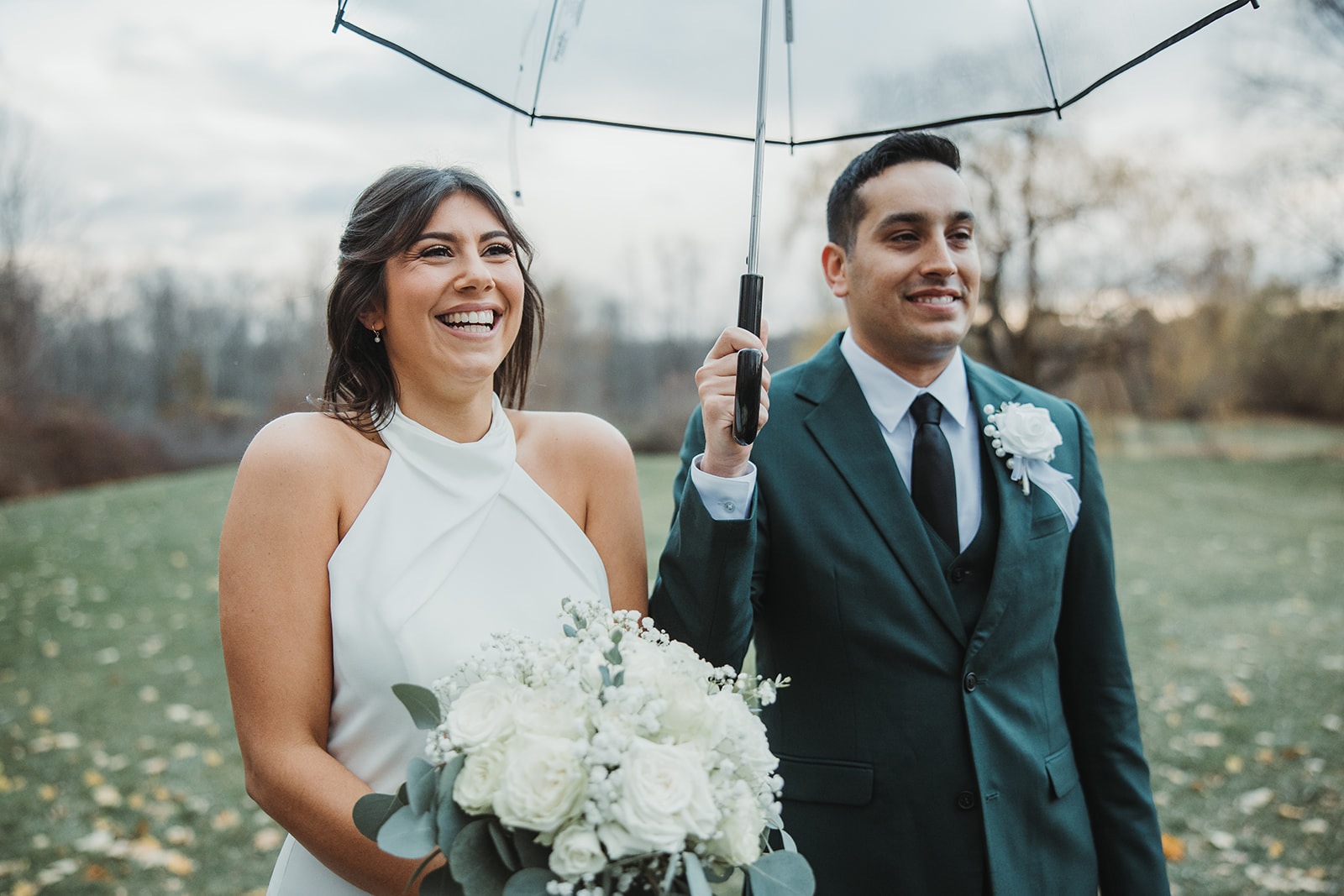 Bride and Groom Walk Under Clear Umbrella During Rainy Wedding