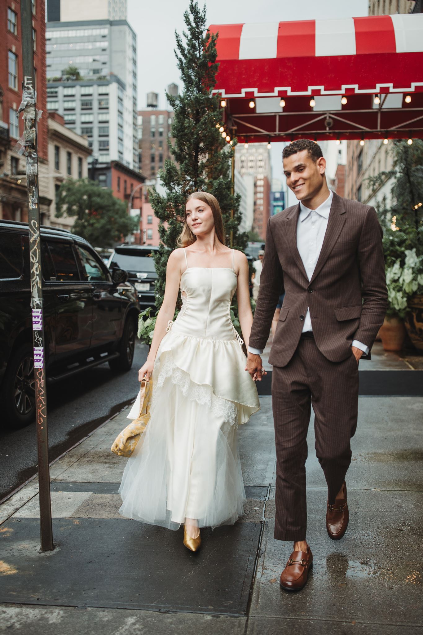 Bride and Groom Hold Hands, Walking on Sidewalk in front of Hotel Chelsea